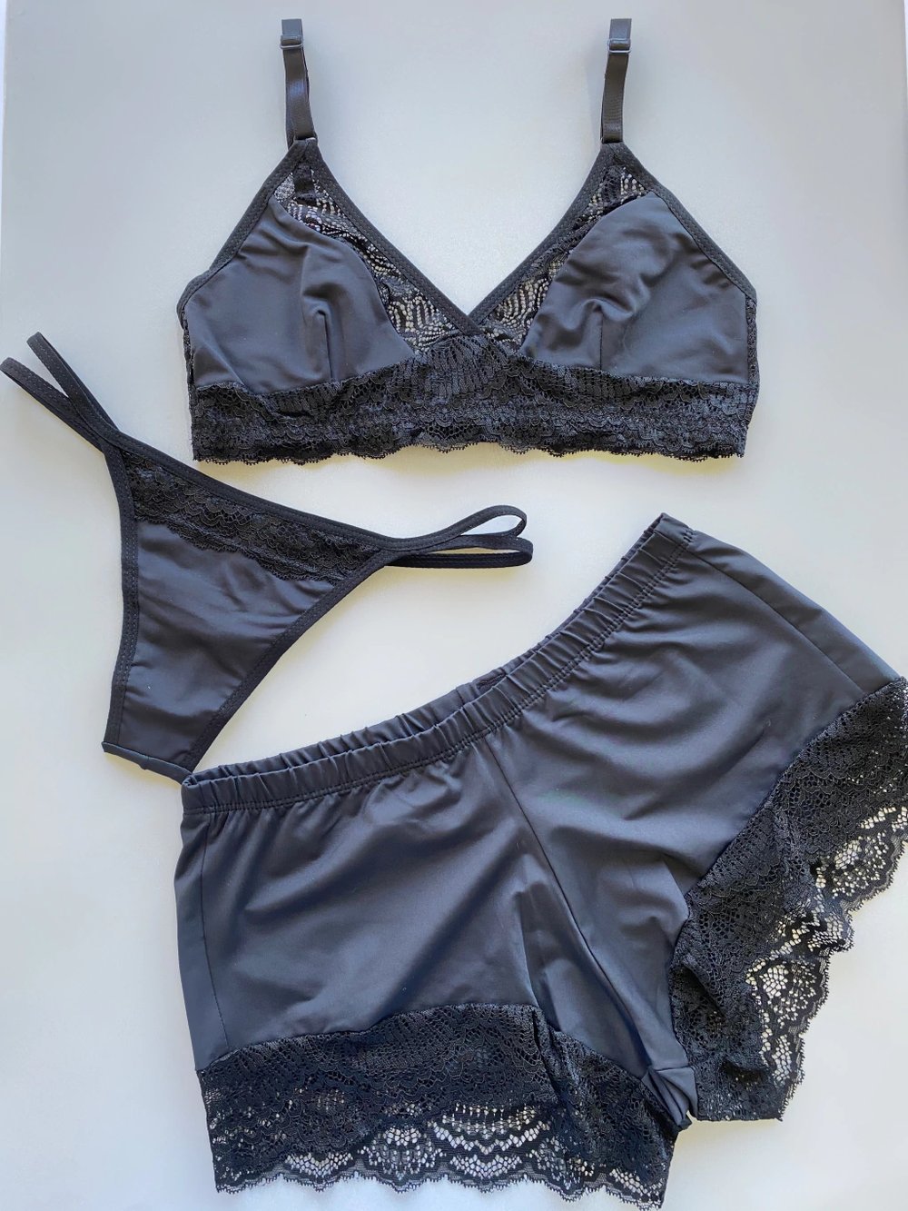 Conjunto 3 peças preto: top de renda, calcinha e short, dispostos sem modelo